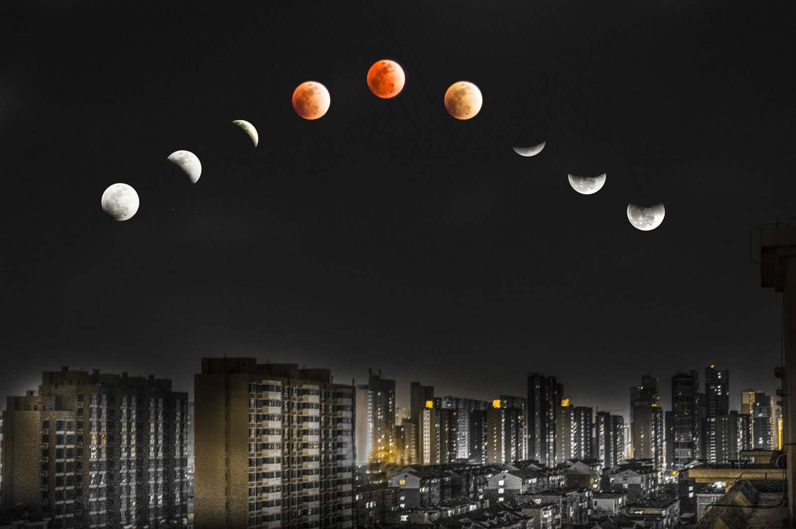 white and red moon over lighted high-rise buildings during night time